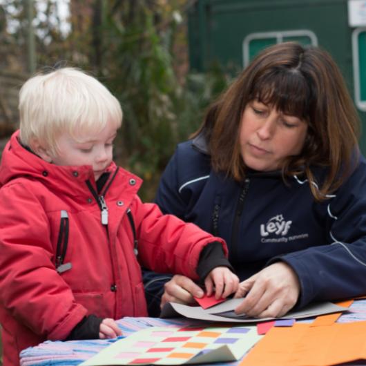 Child making paper art and craft with staff member