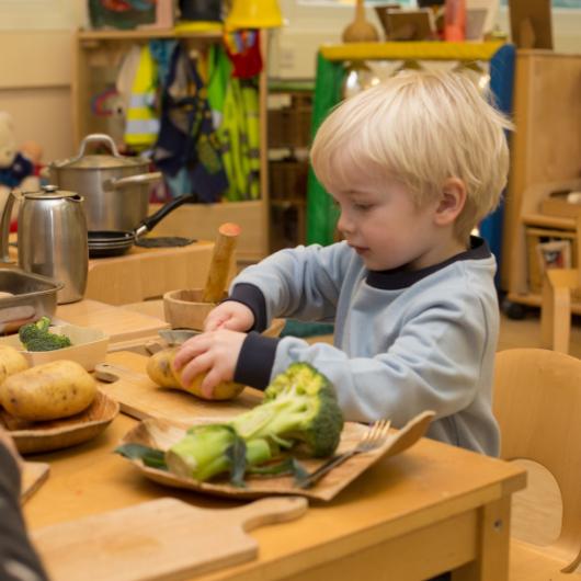 Child in the home corner cutting up some potatoes and vegetables