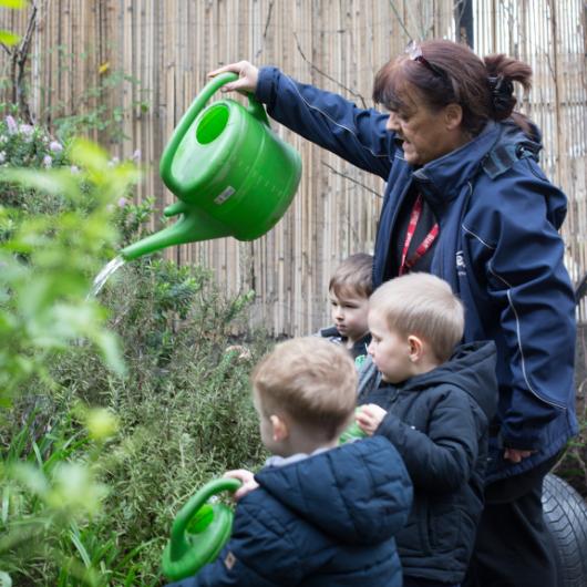 Children watering plants in the garden with staff member