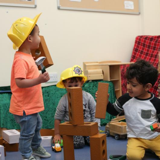 Children building wooden blocks with construction hats on