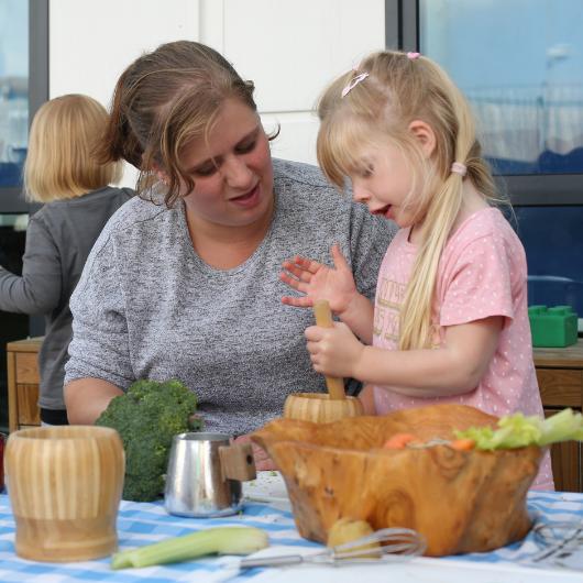 Child playing in the home corner in the garden using cooking objects with staff member