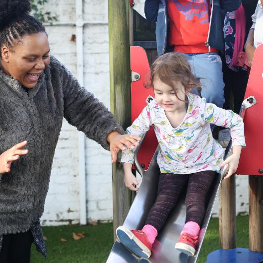 Child going down a slide with staff member helping