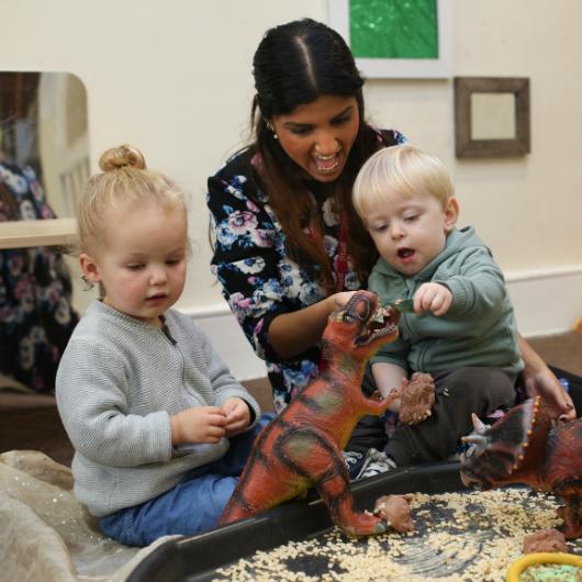 Children playing with dinosaur provocation with staff member