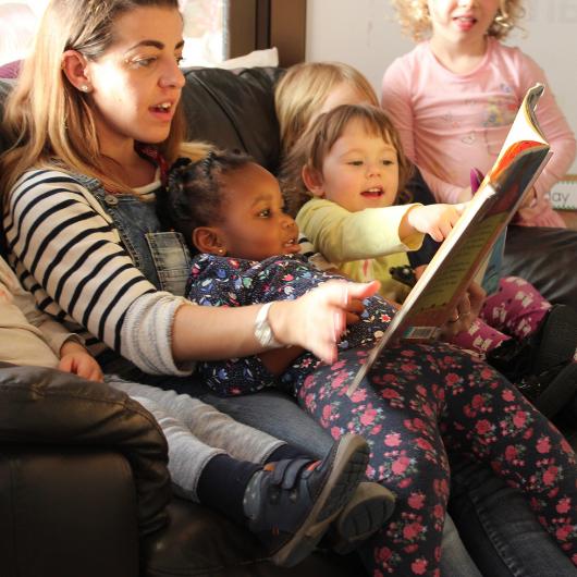 Children and staff sitting very cosy on the sofa reading a book