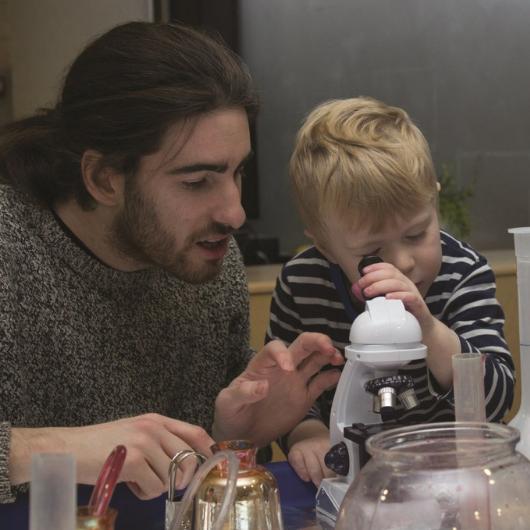 male staff and child doing a science experiment and looking inside the mircoscrope