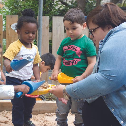 Staff member playing in sandpit with children shoveling sand