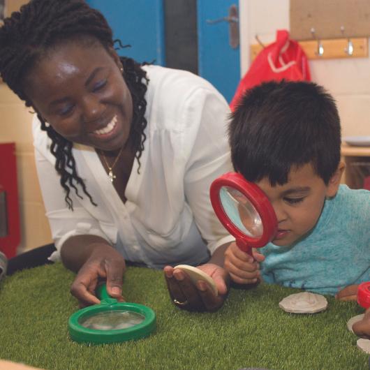 Staff and child using a magnifying glass to look closely at the stone