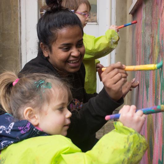 Staff and children painting a wall outside a nursery