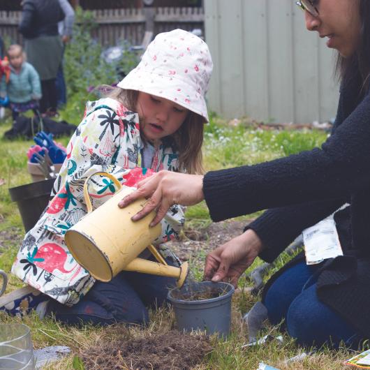 Child and staff member watering plant in the garden