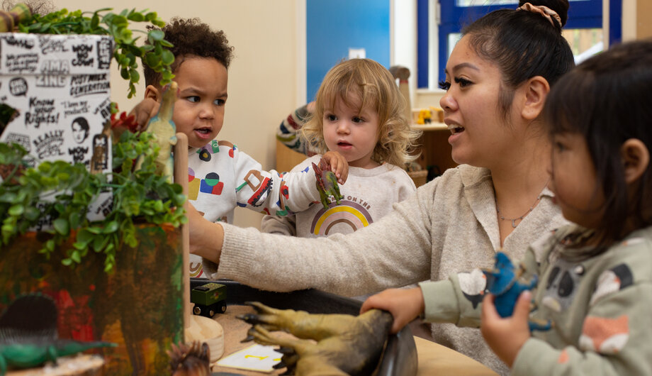 Teacher and children are playing with dinosaurs and exploring natural materials
