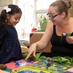 Child painting with leaves with delighted staff admiring the picture