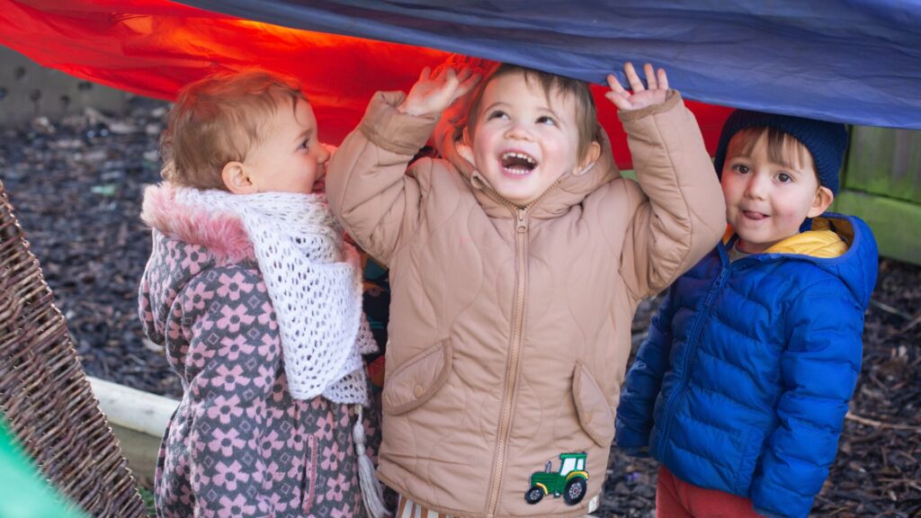 Three children laughing playing under a parachute