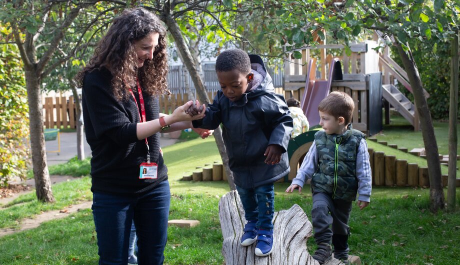 Children walking along a tree stump with teachers help
