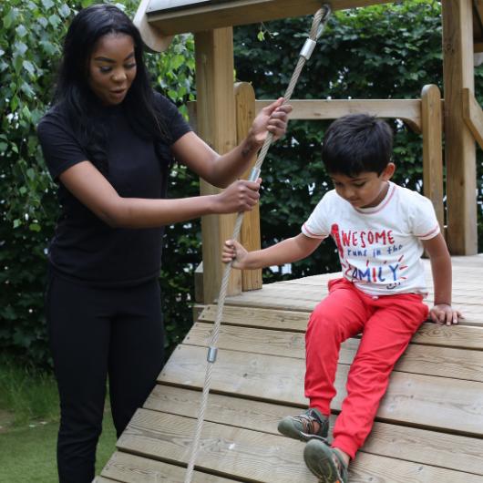 Child playing outside on rope with staff member