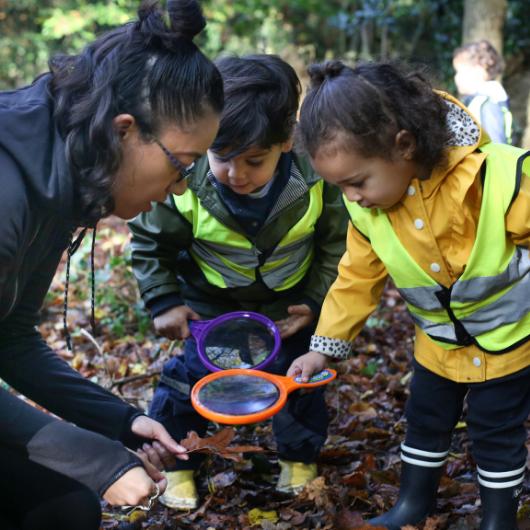 staff and children in the local park exploring and using magnifying glasses to look at the bugs and leaves