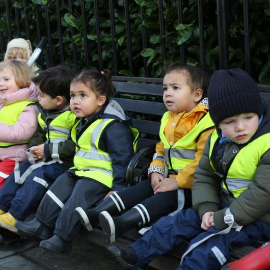 Children sitting in high vis vests on a bench outdoors