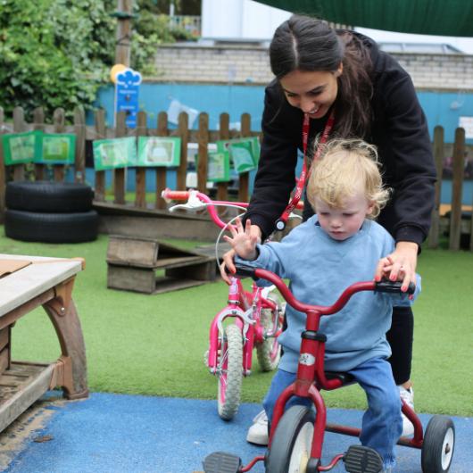 Child riding a bike with staff member holding handlebars