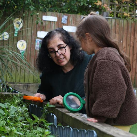 Child and staff member outside with magnifying glasses in garden