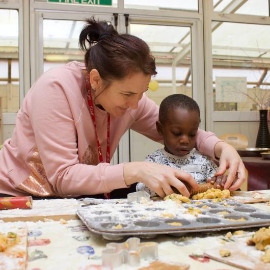 Staff member helping child prepare dough