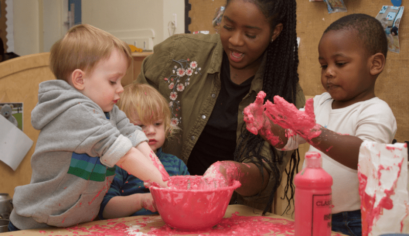 Children enjoying messy play with a teacher by putting their hands in paint
