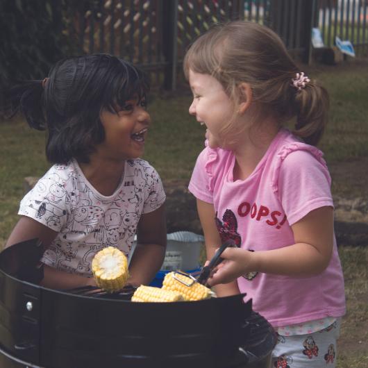 Children putting sweetcorn on toy barbeque and laughing