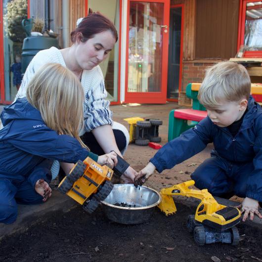 Children playing with diggers in mud with teacher