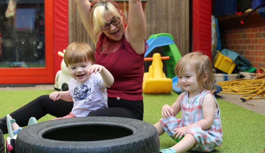 Children and teacher playing with tyre in nursery garden