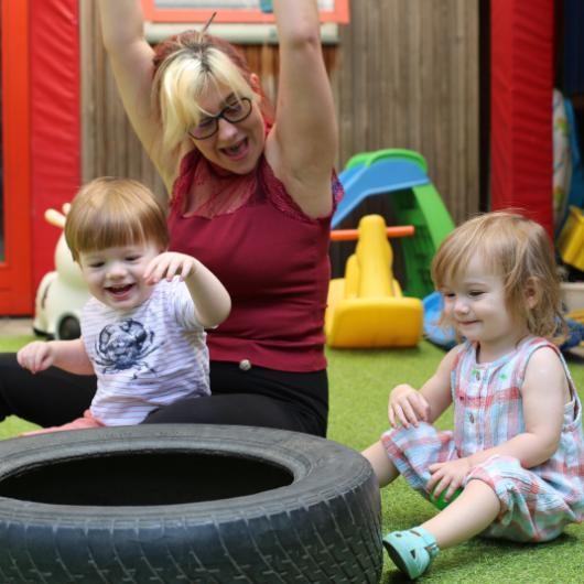 Children and teacher playing with tyre in nursery garden