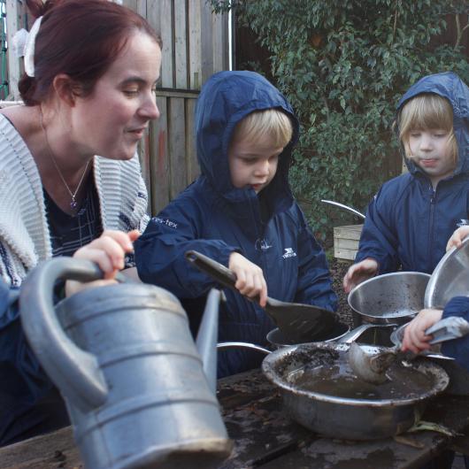 Children and teacher in garden with bowls of mud