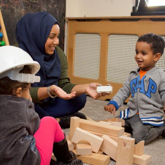 Nursery teacher and children constructing tower from wooden blocks