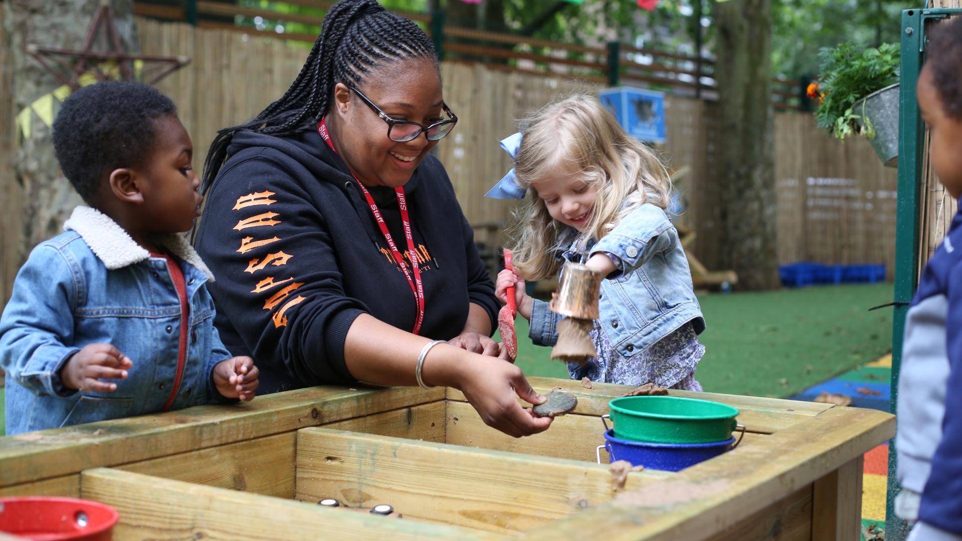 Children and nursery teacher play in the sandpit