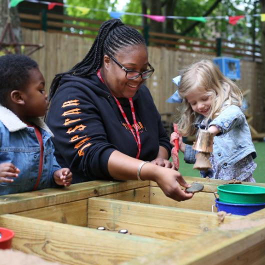 Children and nursery teacher play in the sandpit