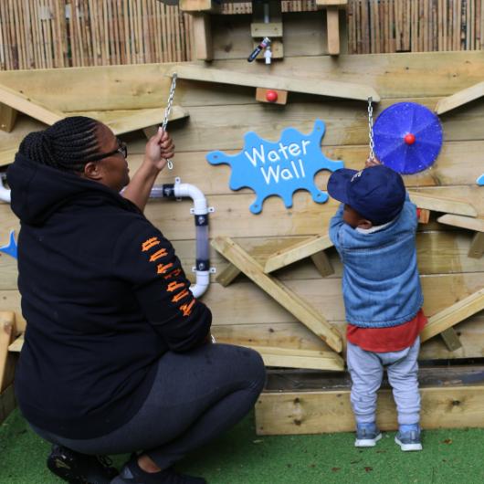 Child plays on the nursery water wall in the garden