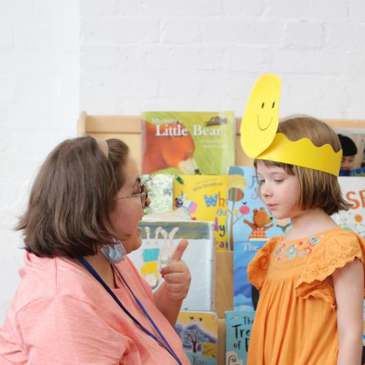 Girl wearing smiley face hat and teacher gives thumbs up