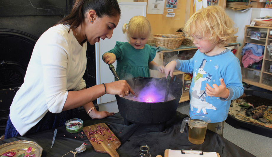 Children and nursery teacher do potion making science experiment with cauldron