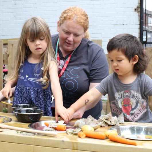 staff and children playing in the outdoor home corner using tea bags and vegetables