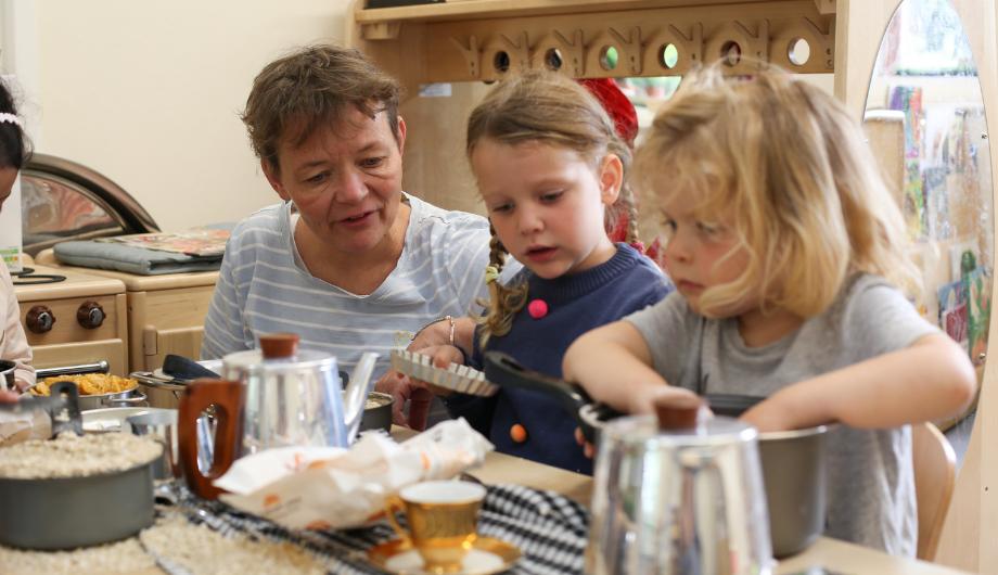 children and staff playing in the home corner, pretending to cook and bake