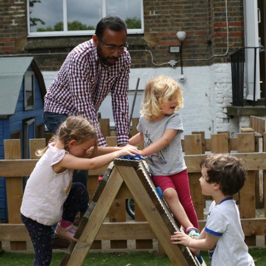 Male staff and children doing some risky play, climbing a frame