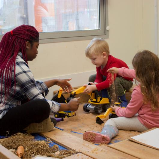 Staff and children playing with trucks and sand, doing some construction