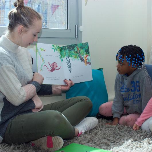 staff reading a book to two children while sitting on the carpet