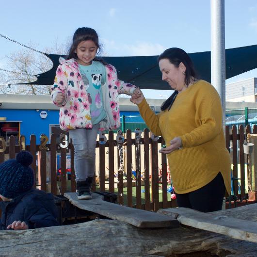 Staff helping a child cross a wooden plank, practicing risky play