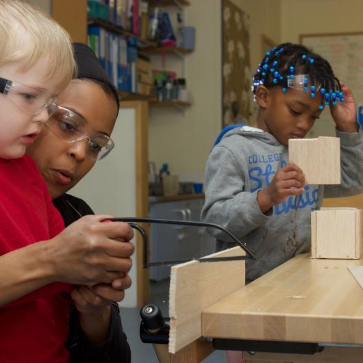 Staff and children doing some wood works, by sawing some wood. Learning to be safe by using goggles