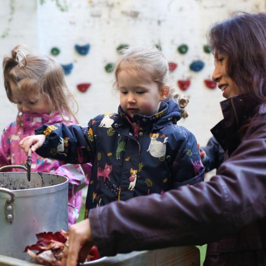 Children and staff playing the the muddy kitchen outside in the garden making something out of mud and water