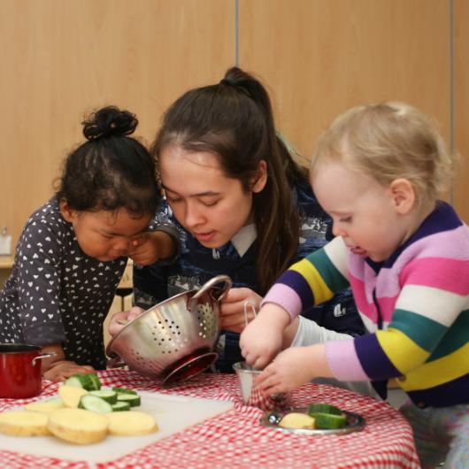 staff and children cutting vegetables and fruit in the home corner