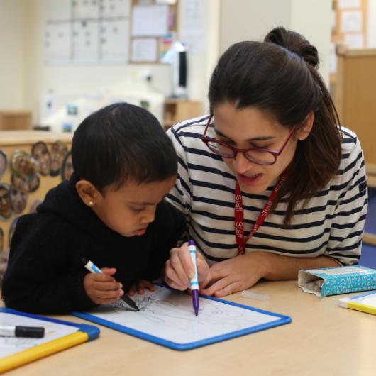 Children and staff drawing on a white board with markers