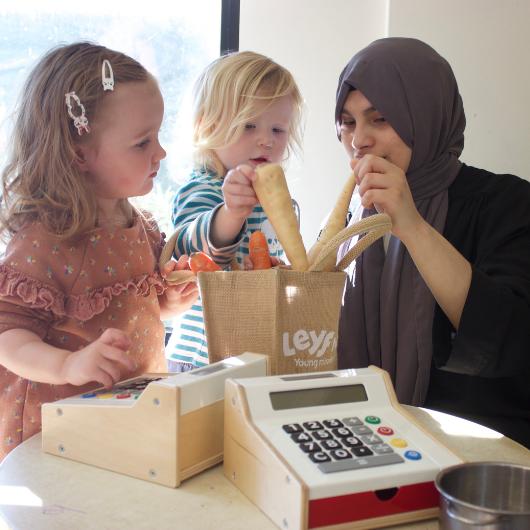 Staff and children pretending to buy vegetables at their local shop