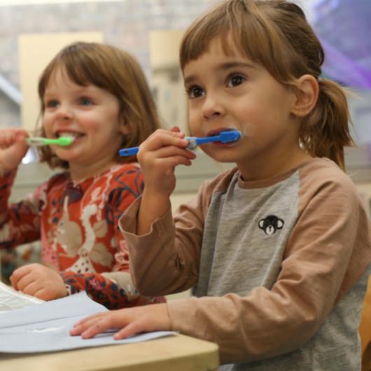 Two children practicing how to brush their teeth after lunch