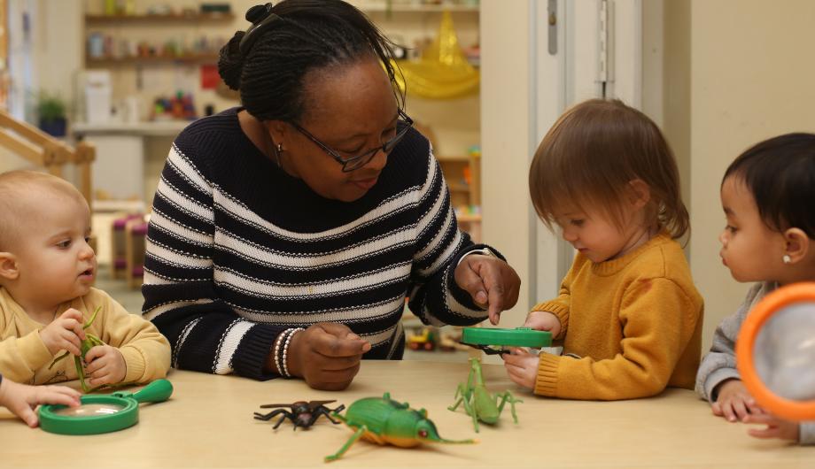 Member of staff looking at small insects with a magnifying glass with a child
