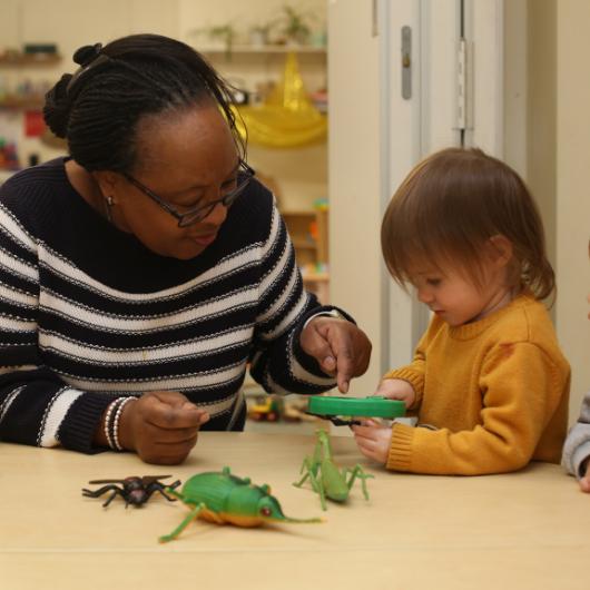 Member of staff looking at small insects with a magnifying glass with a child