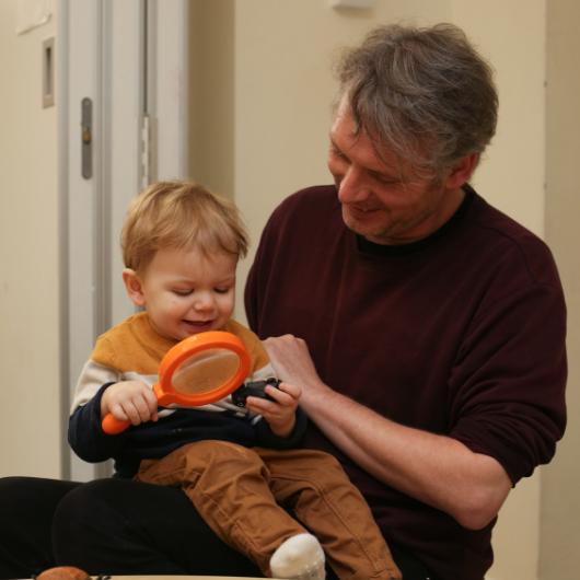 A male member of staff looking at small insects with a magnifying glass with a child